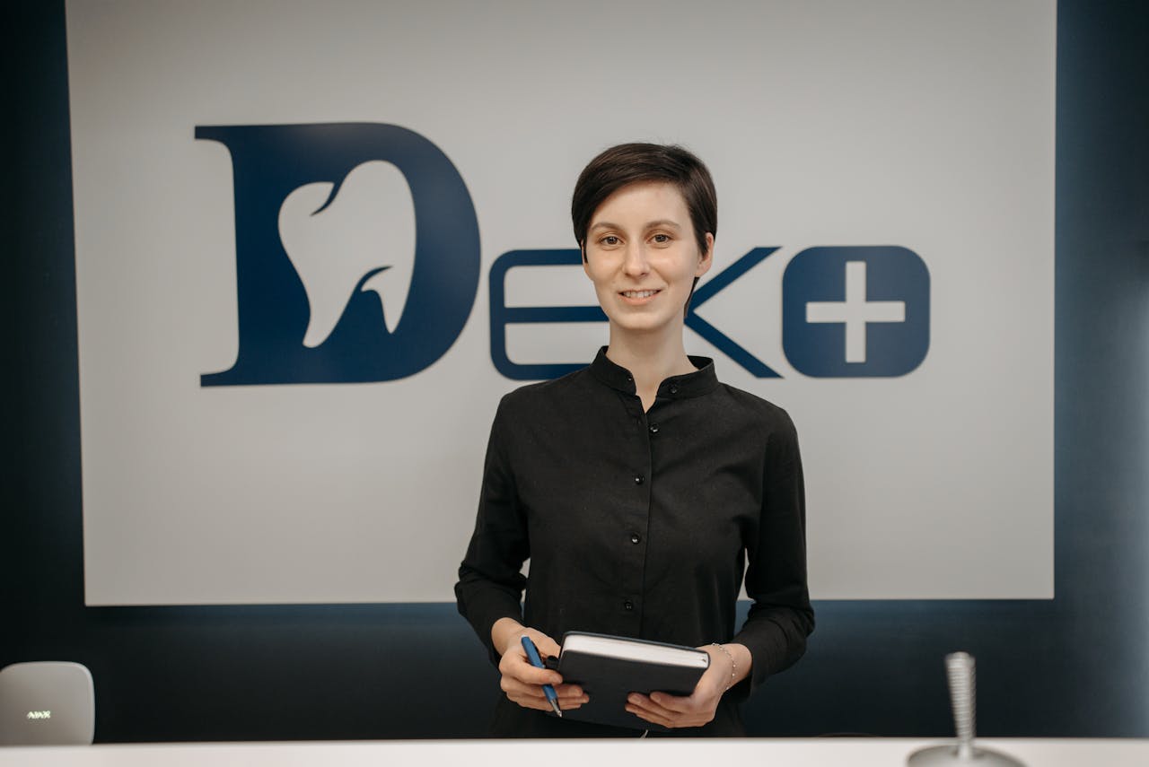 Smiling dentist holding a notebook in front of a clinic sign, promoting a welcoming and professional dental environment.